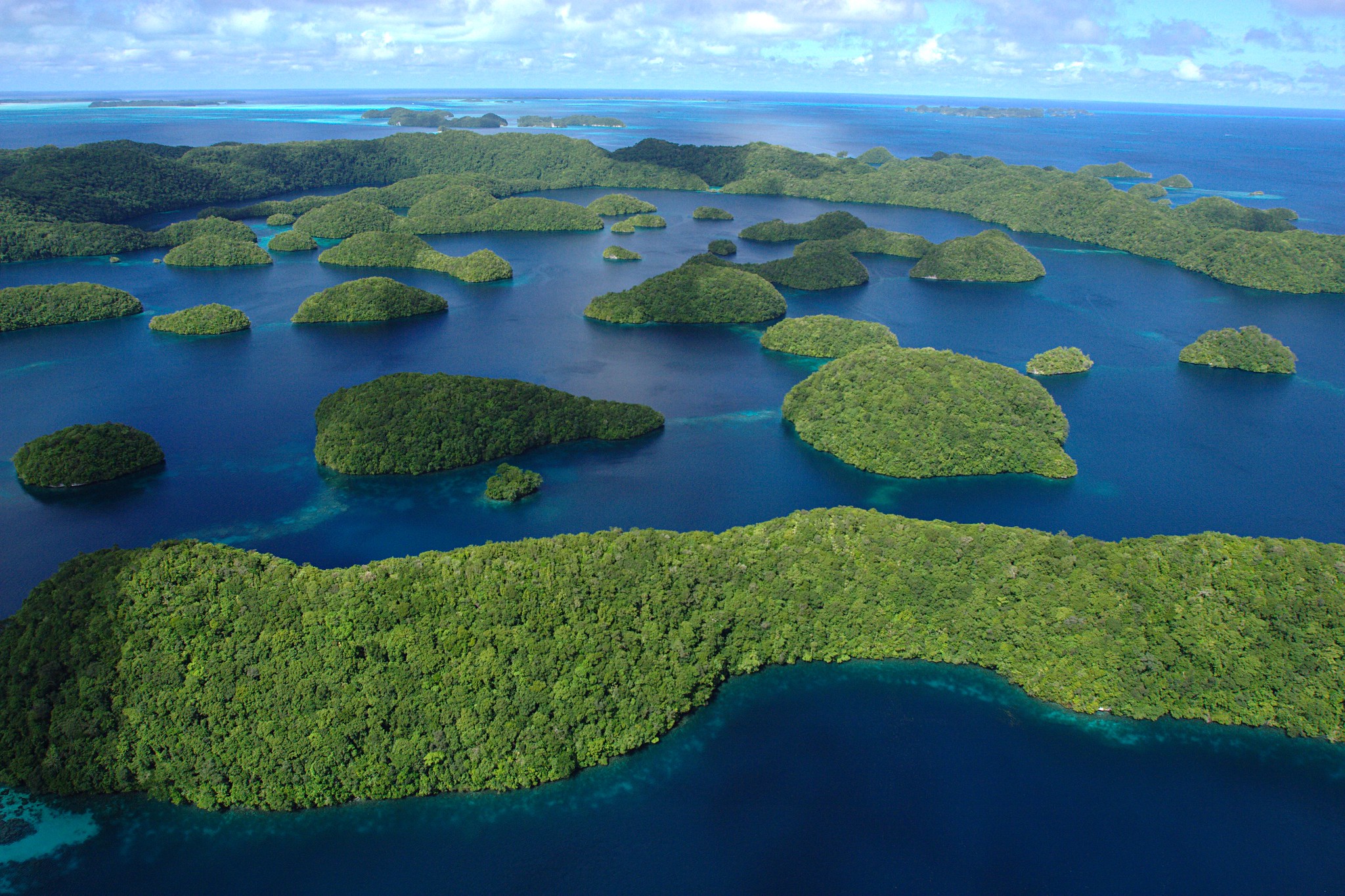 Aerial photo of an archipelago of small, plant-covered islands in a deep blue ocean.