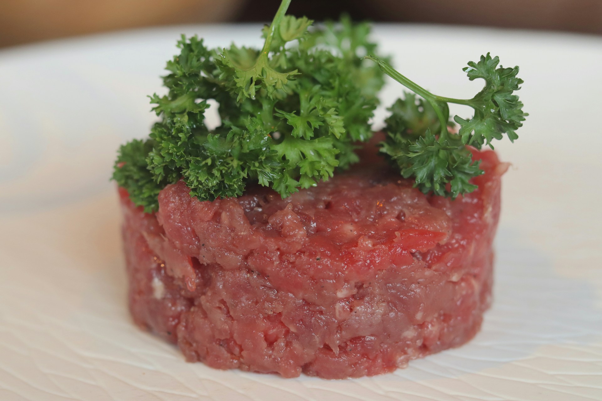 Photo of simple beef tartar, garnished with a sprig of parsley.