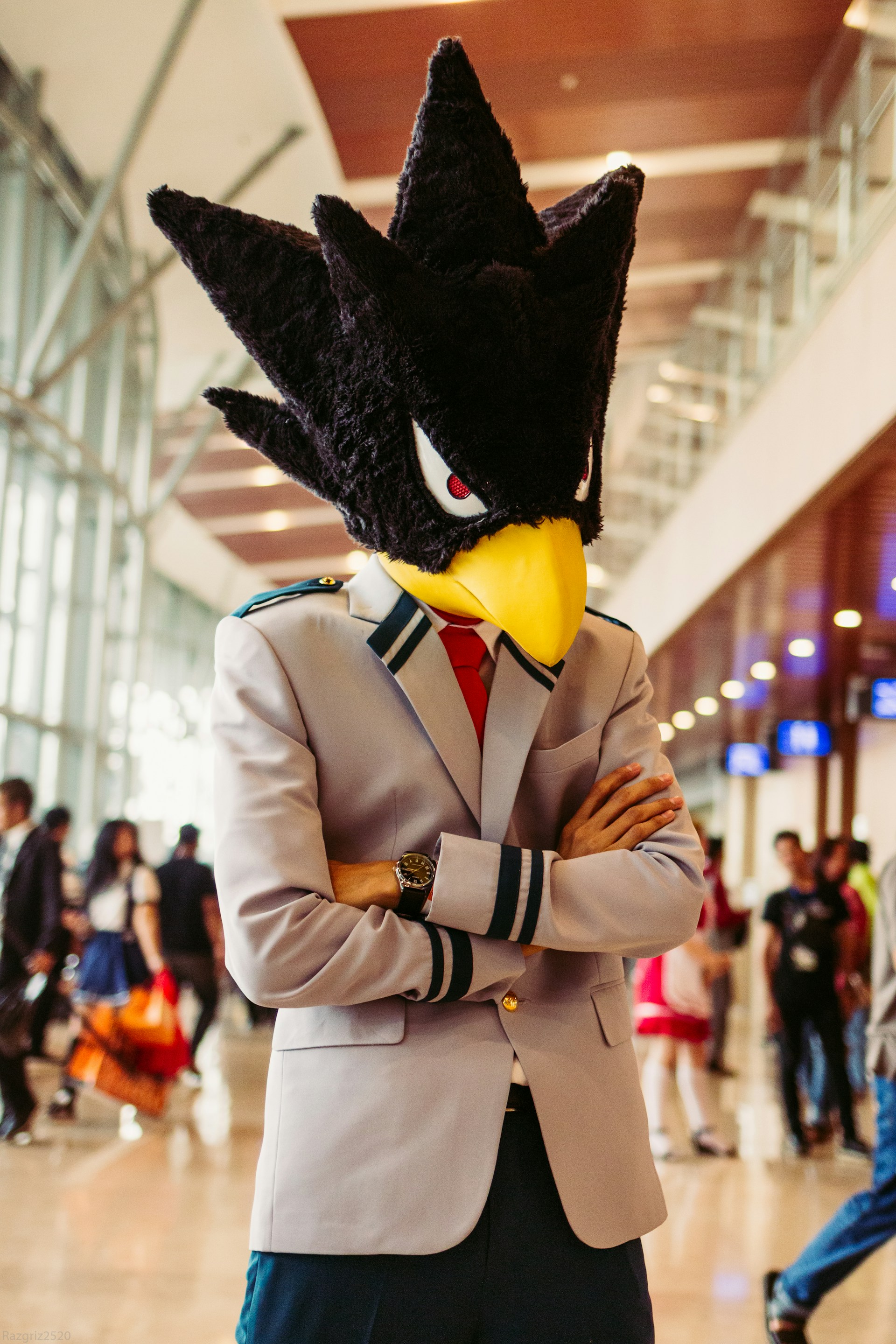 Photo of a person dressed in a pilot's outfit, wearing a large mascot head shaped like a scowling bird with black spikey feathers.