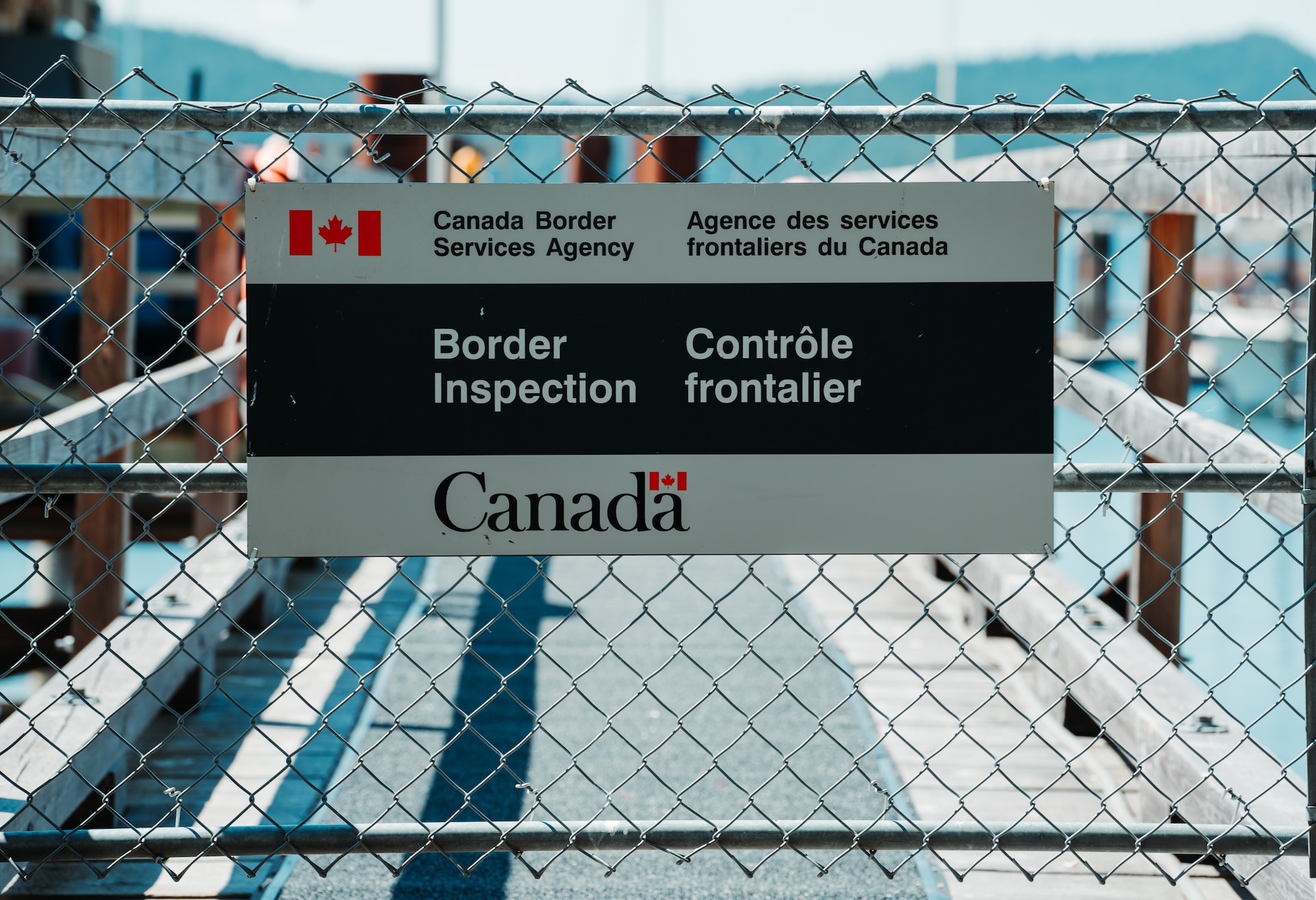 A sign on a fence that says 'Canada Border services Agency -- border inspection' and 'Agence des services frontaliers du Canada - Contrôle frontalier'