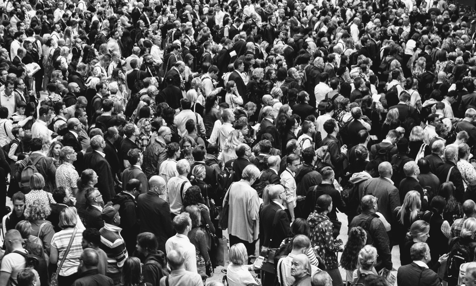 Black and white photo of a crowd of people, mainly facing in the same direction away from the camera.