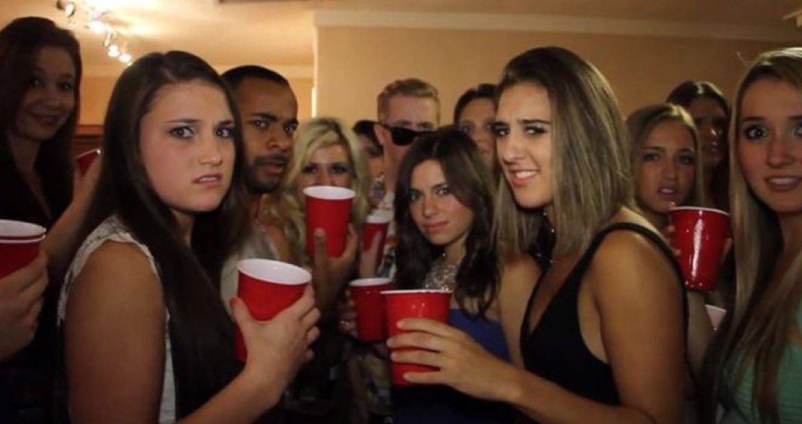 Photo of a college party. Frame is crowded with people holding red Solo cups. They are all looking at the camera with expressions of disgust, surprise, and confusion on their faces.
