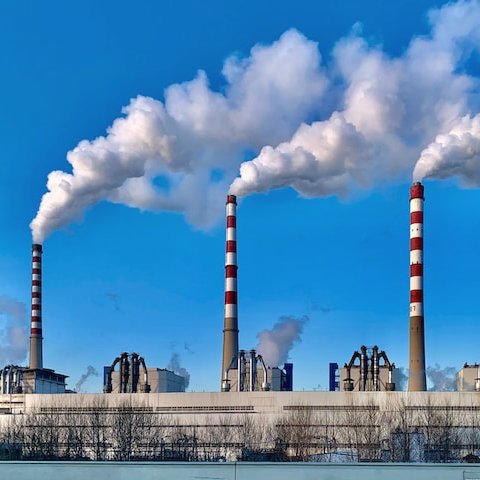 Photo of a factory with three stacks releasing large plumes of white steam.