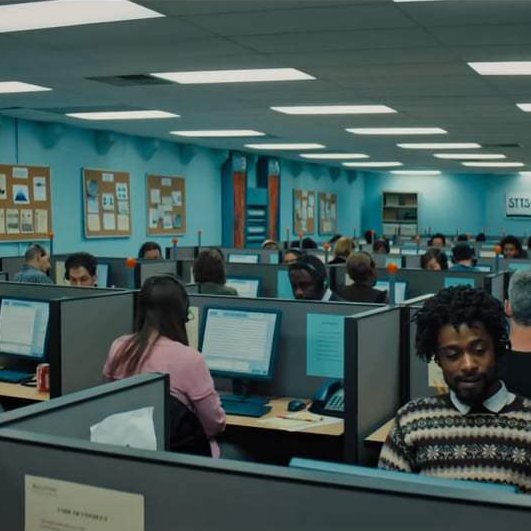 Still from Sorry to Bother You (2018) depicting a man looking resigned and aprehensive in large room filled with cubicles.