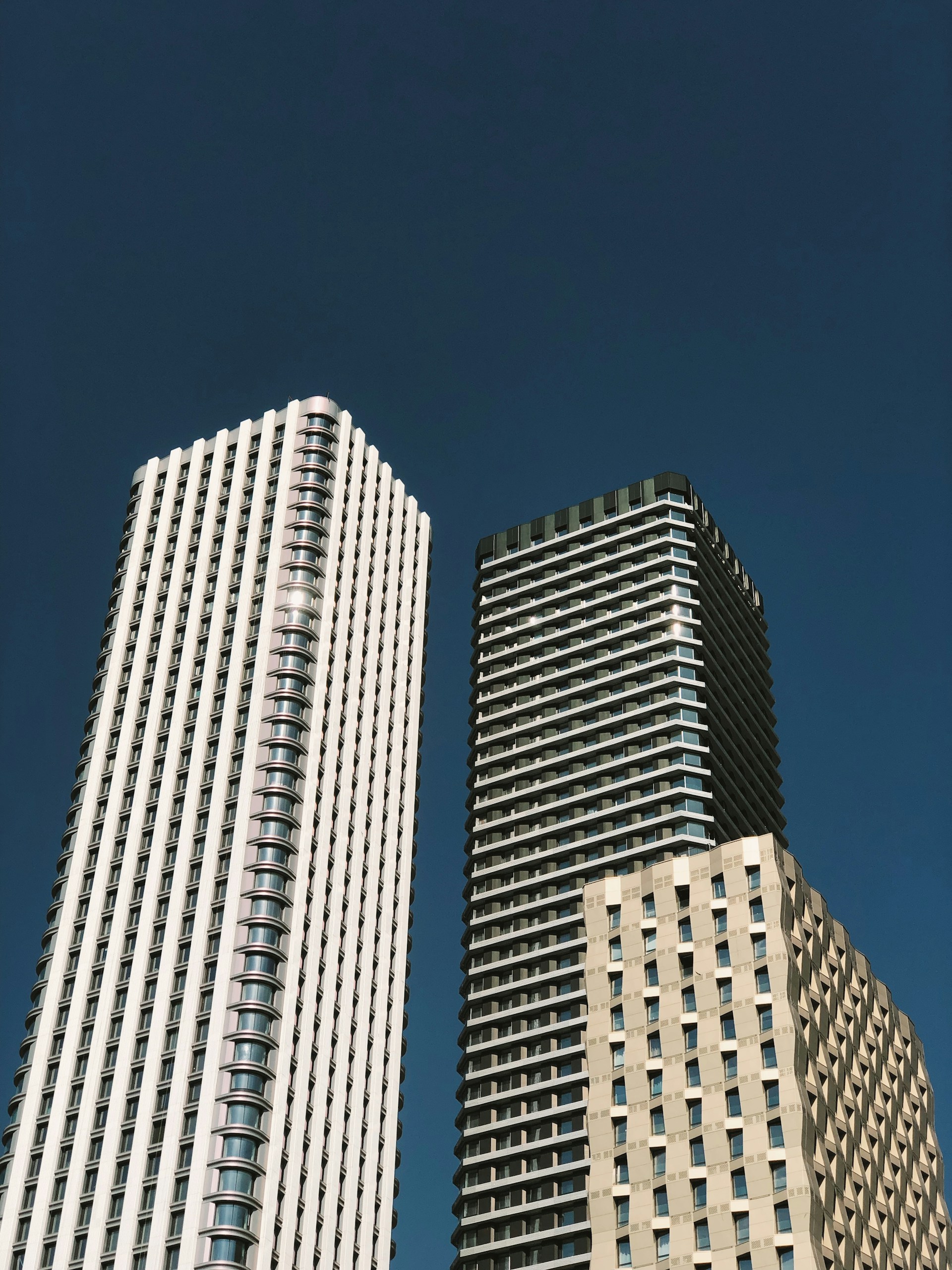 Low-angle photo of three bland office towers against a dark blue sky