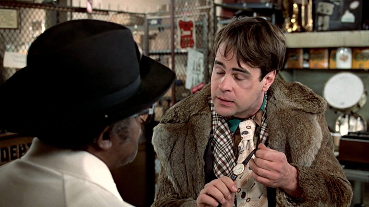 Still from Trading Places. A white man in a fur coat that appears to have been nice but is now shabby presents a watch to a Black pawn shopo owner