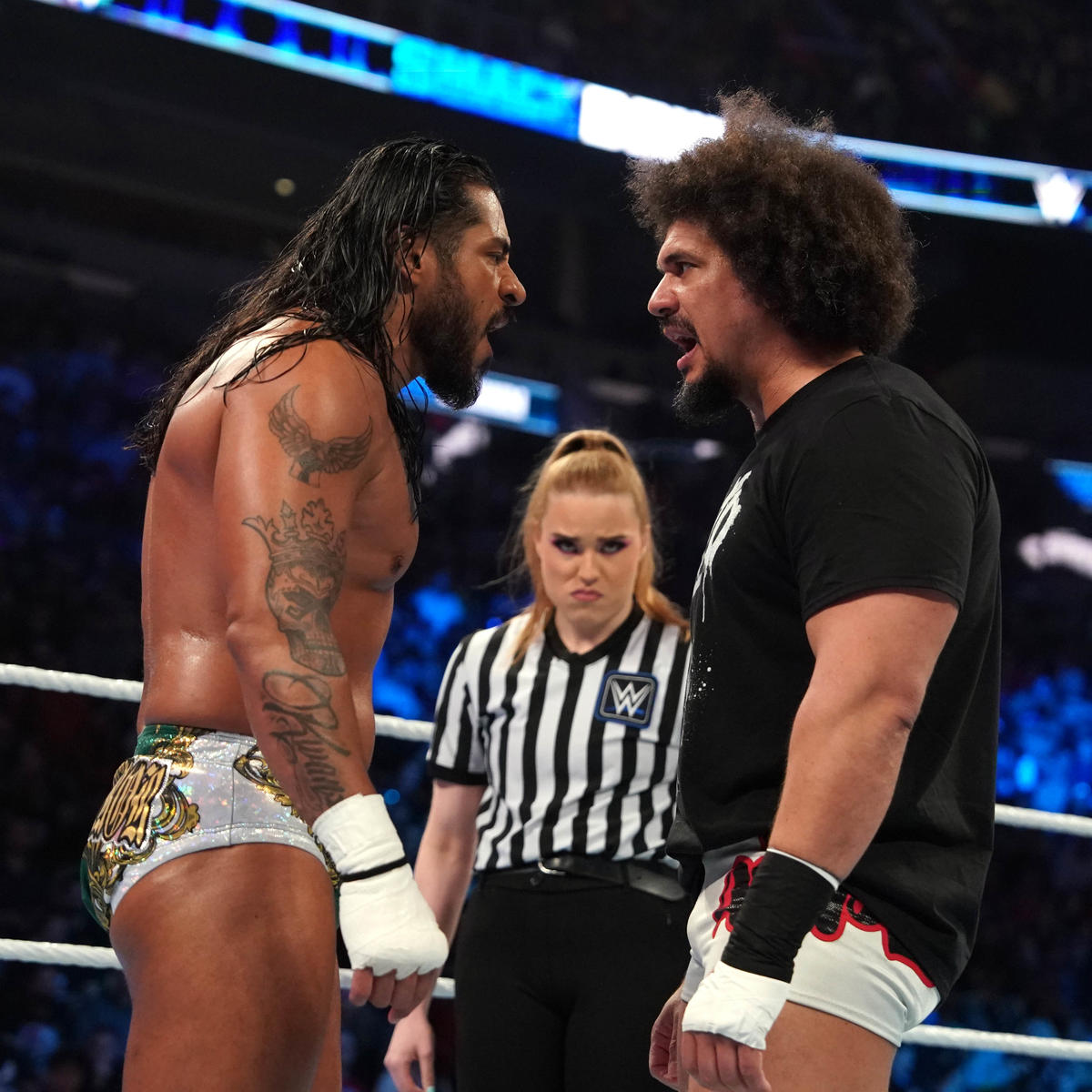 Two WWE wrestlers looking angrily at each other before a match. The referee stands in the background scowling.