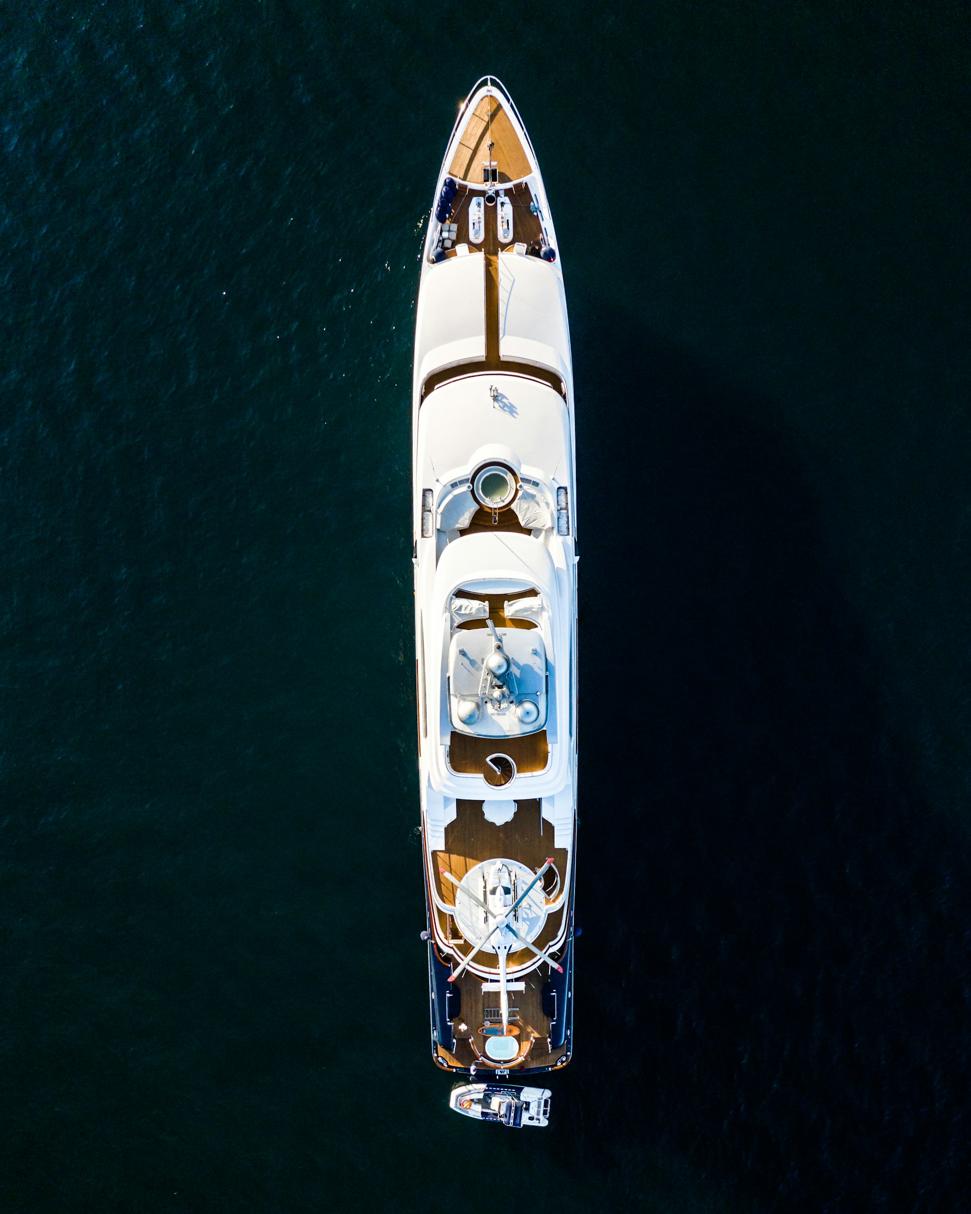 Photo of a large yacht in dark water from directly above. The yacht features a parked helicopter and attached motorboat.
